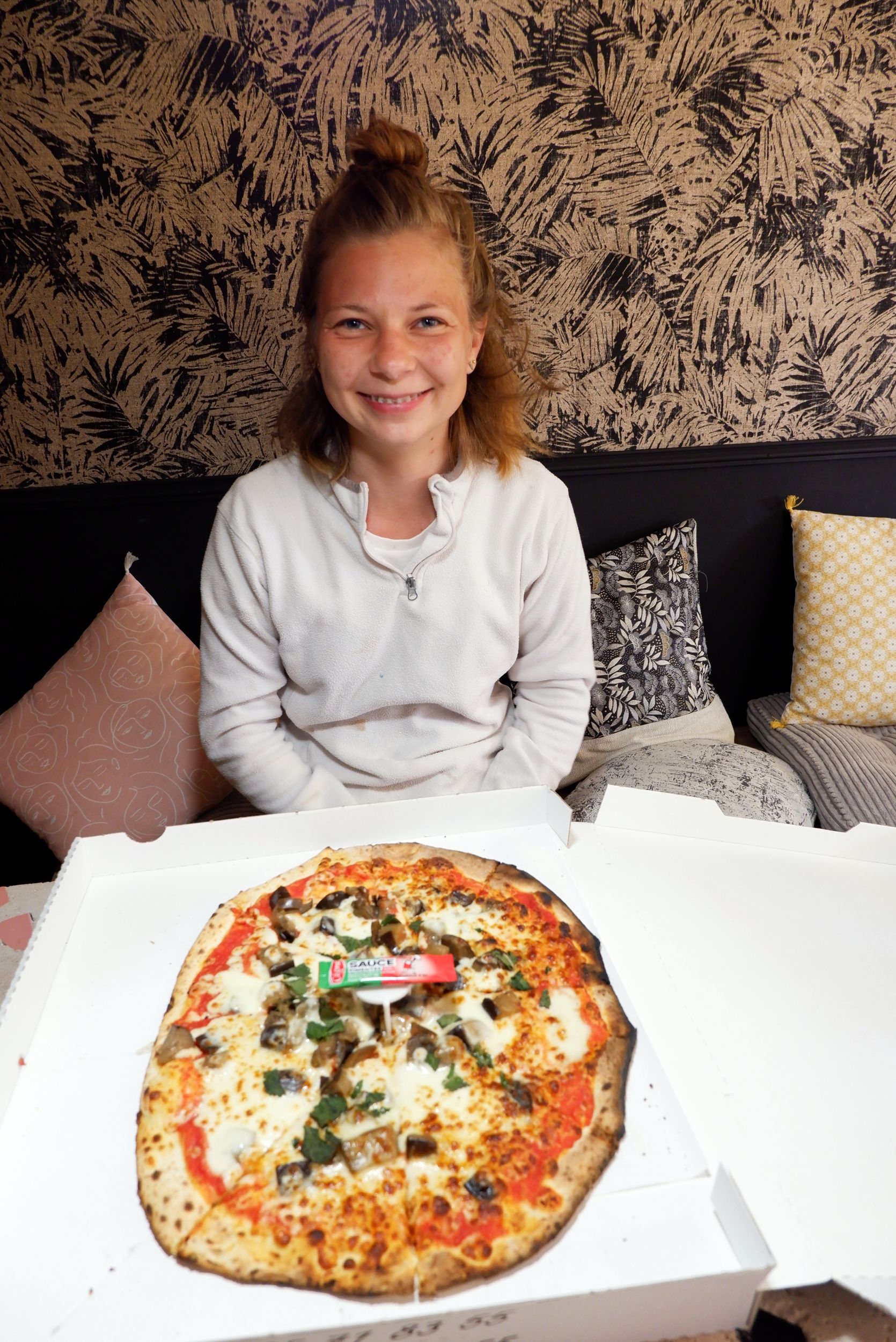 Justine sourit devant une pizza.