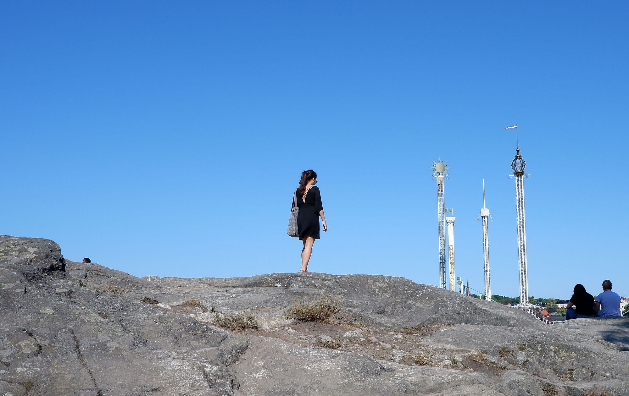 Marina se promenant sur un chemin rocheux en face d'un parc d'attraction.