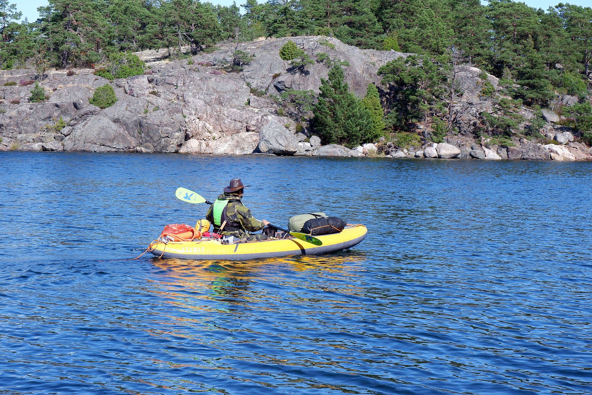 Un homme sur un kayak gonflable jaune avec plein de sacs et un chien allongé 